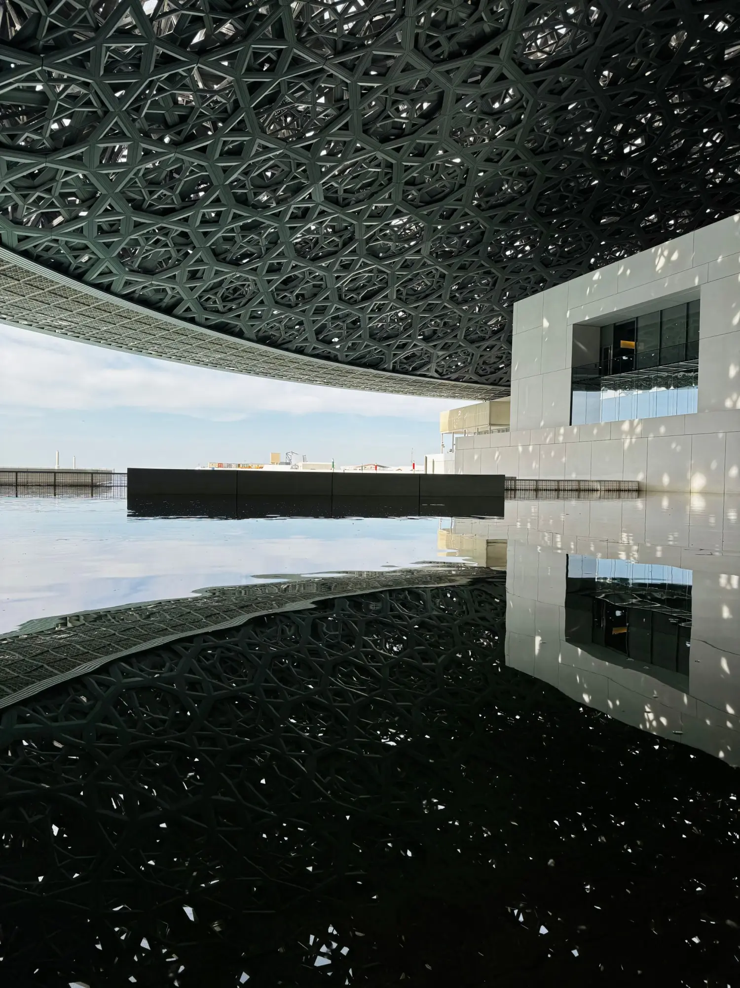 The geometric canopy of Louvre Abu Dhabi mirrored in still water