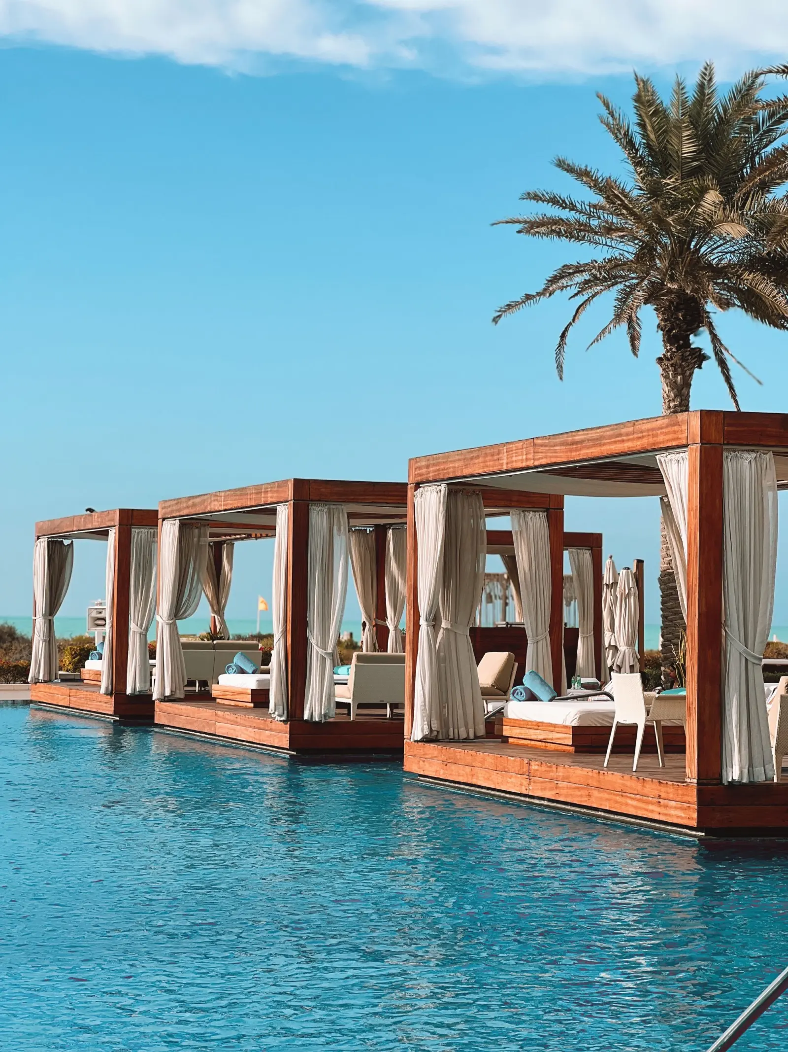 Timber cabanas beside a pool and palms at a Saadiyat Island beach club